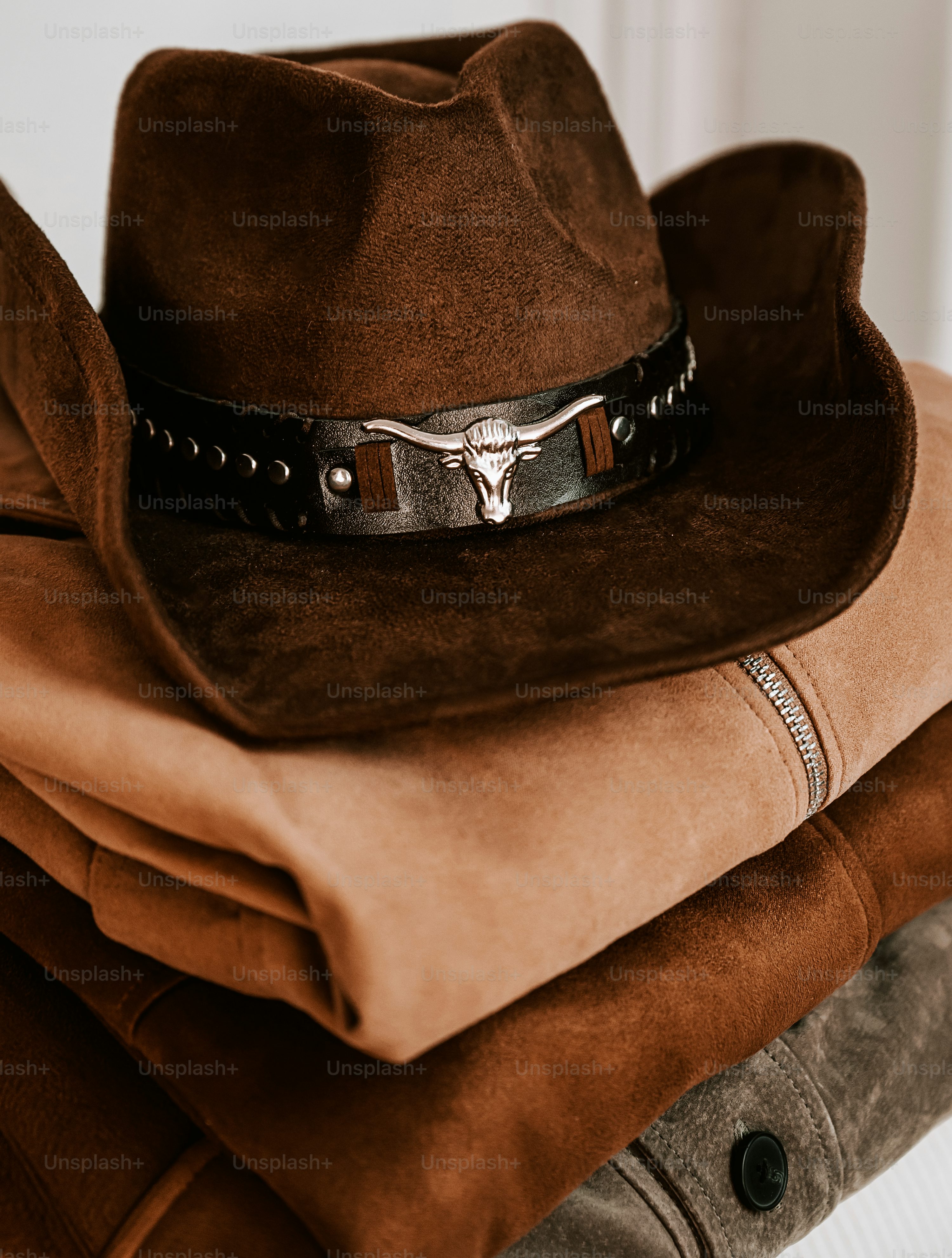 A brown cowboy hat with a silver bull emblem on folded jackets